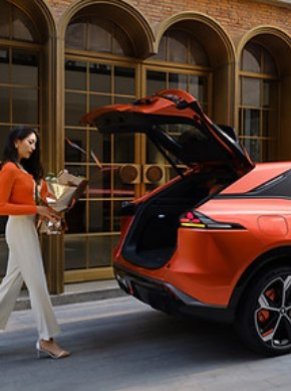 Woman placing items in the boot of an orange car with the tailgate open.