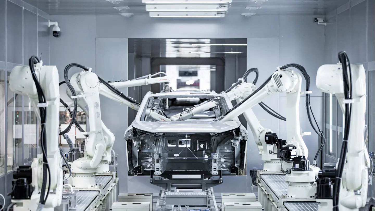 Robotic arms assembling a car chassis in a factory setting.