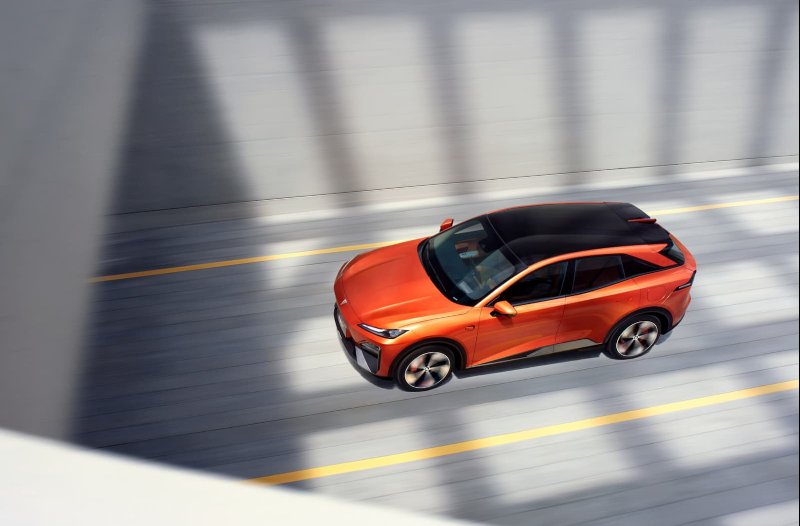 Orange car driving on a road, viewed from above.