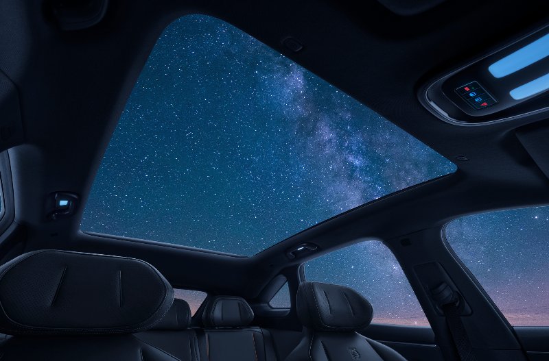 Car interior with panoramic sunroof displaying starry night sky.