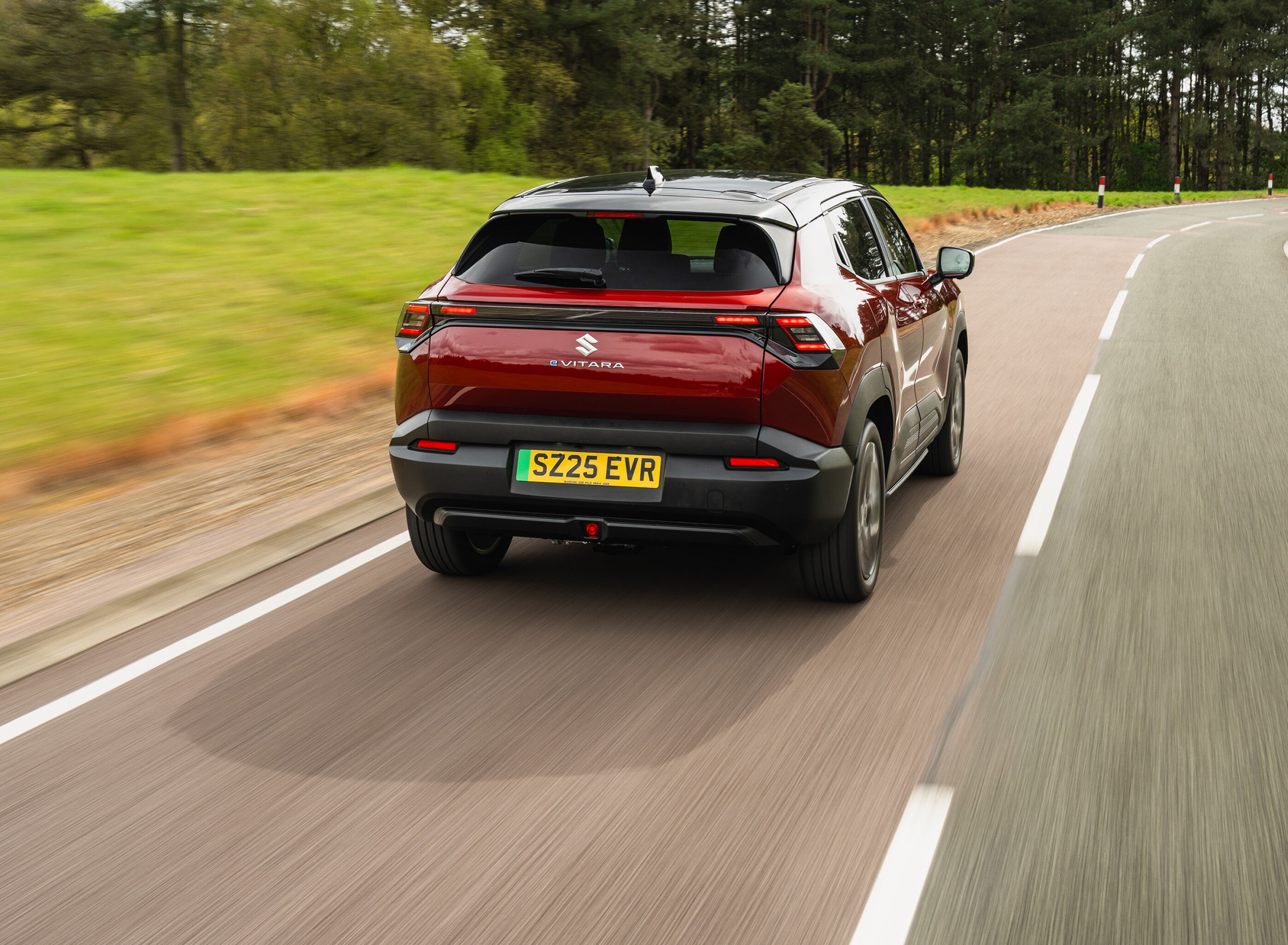 Rear view of a red Suzuki e-Vitara driving on a road.