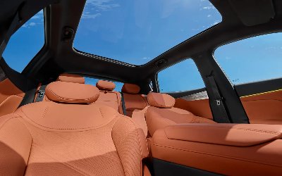 Car interior with orange leather seats and panoramic sunroof under a blue sky.