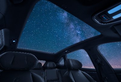 Car interior with panoramic sunroof showing a starry night sky.