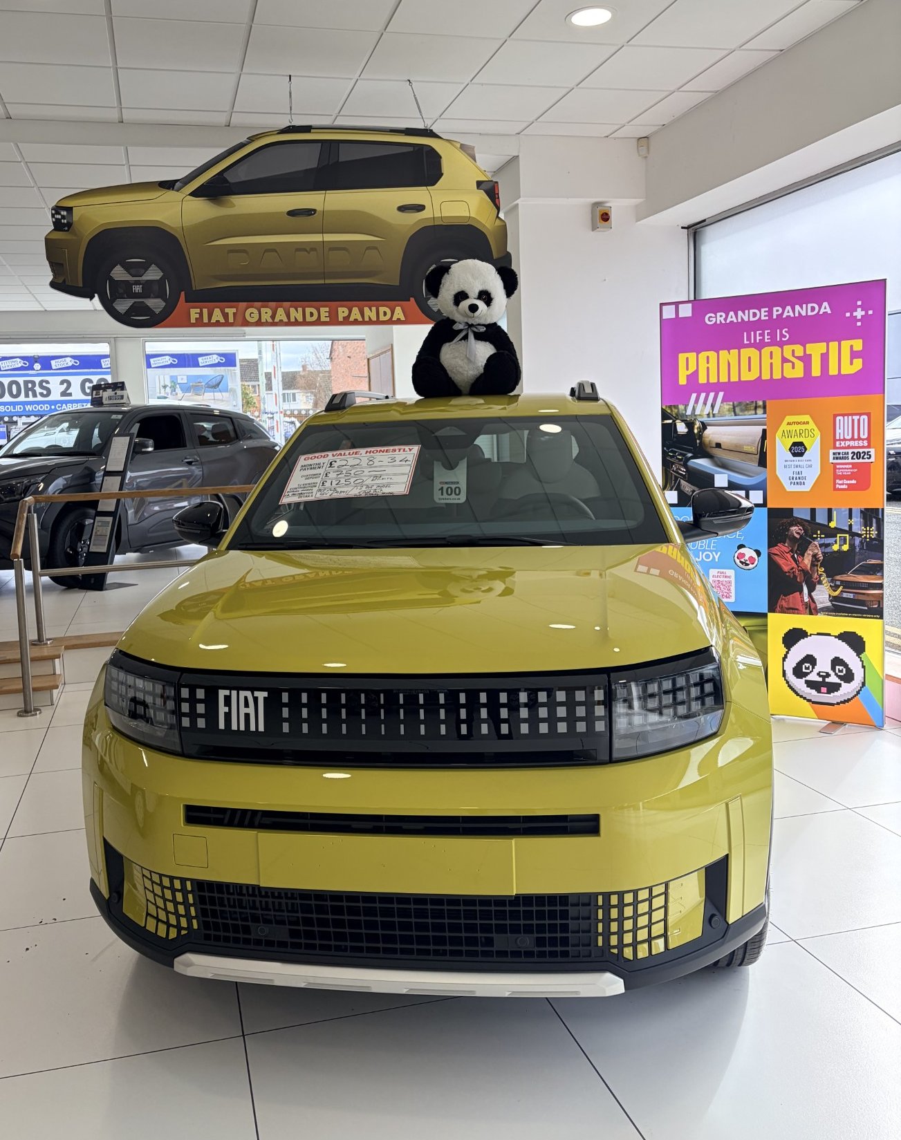 Yellow Fiat car with a panda toy on the bonnet in a showroom.